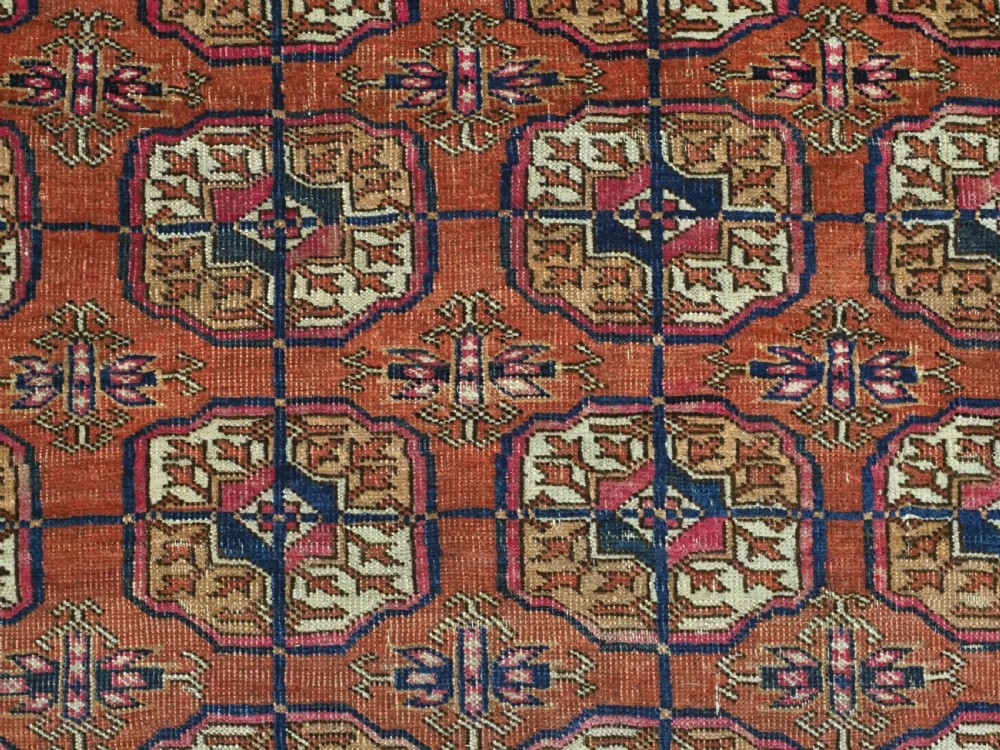 An antique Tekke Turkmen hand-knotted wool rug featuring repeating octagonal gul motifs on a deep brick red background with geometric borders. View VII