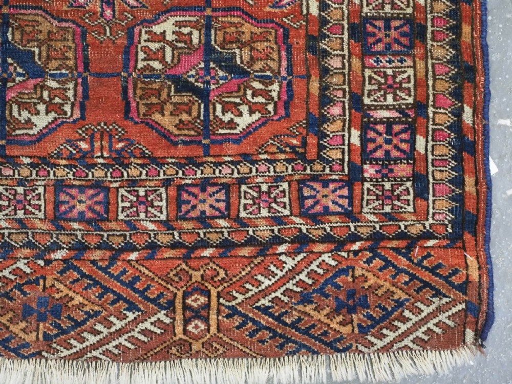An antique Tekke Turkmen hand-knotted wool rug featuring repeating octagonal gul motifs on a deep brick red background with geometric borders. View IX