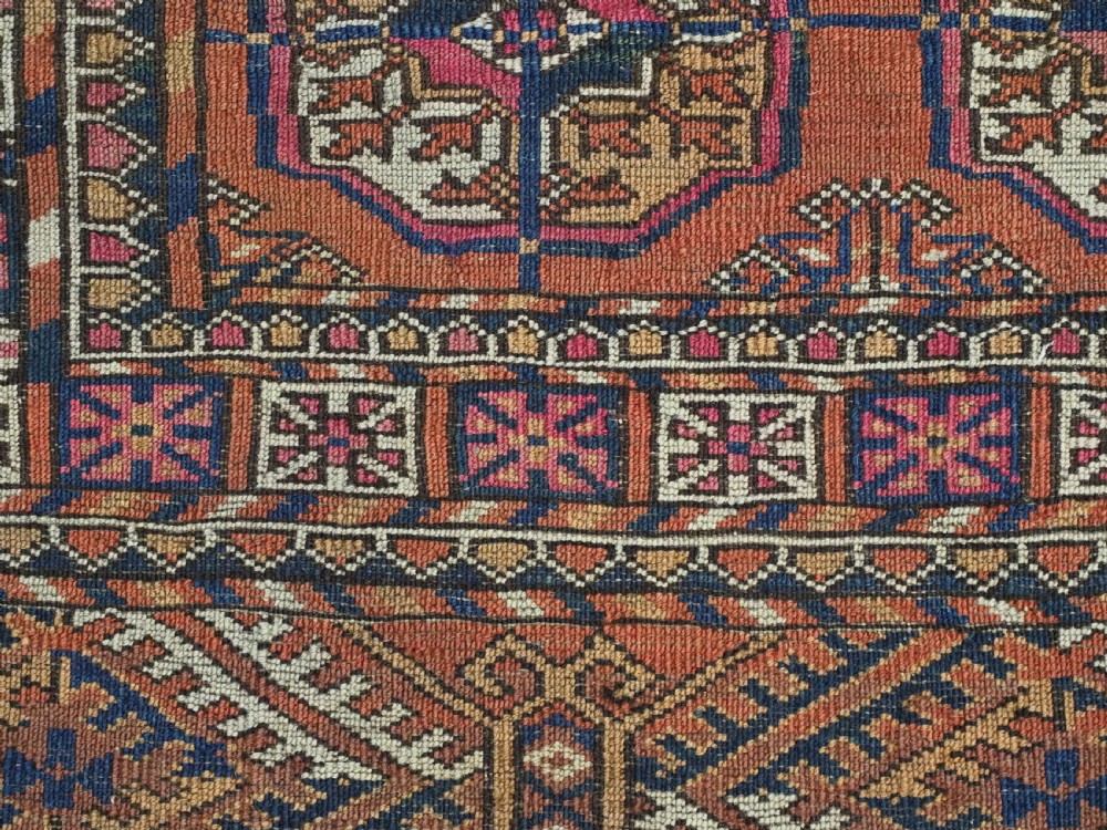 An antique Tekke Turkmen hand-knotted wool rug featuring repeating octagonal gul motifs on a deep brick red background with geometric borders. View X