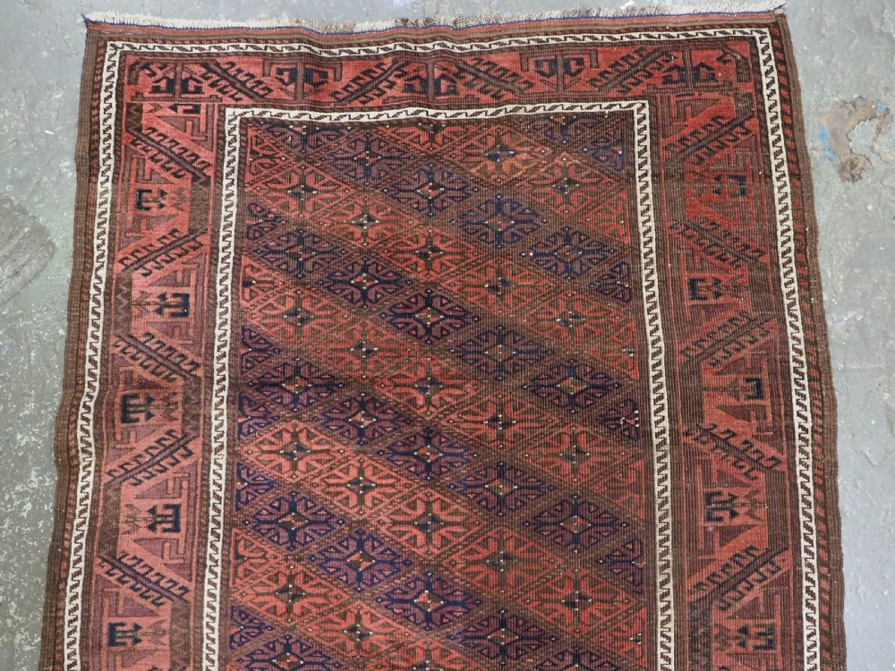 An antique 19th-century Khorasan Baluch wool rug featuring a repeating diamond calyx lattice pattern in rust red, dark navy, and brown with geometric borders. View III