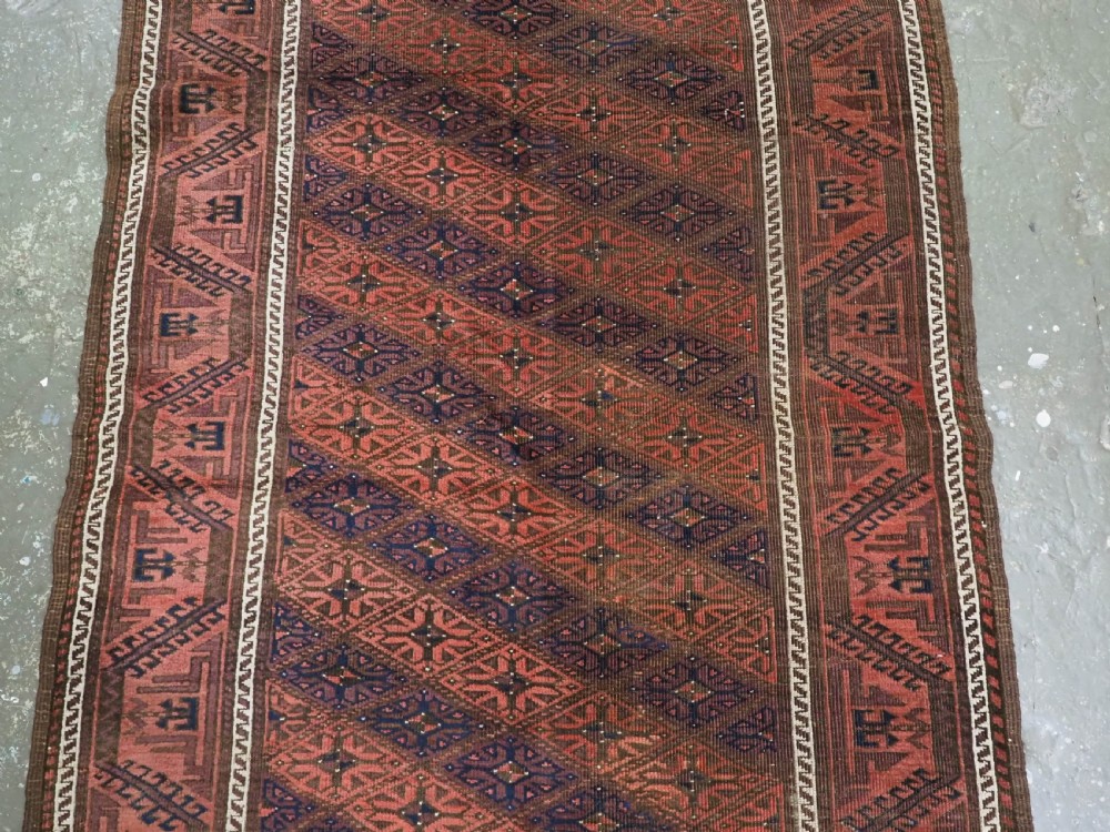 An antique 19th-century Khorasan Baluch wool rug featuring a repeating diamond calyx lattice pattern in rust red, dark navy, and brown with geometric borders. View IV
