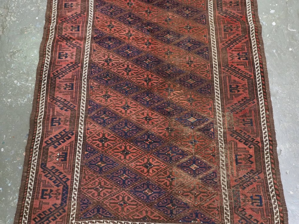 An antique 19th-century Khorasan Baluch wool rug featuring a repeating diamond calyx lattice pattern in rust red, dark navy, and brown with geometric borders. View V