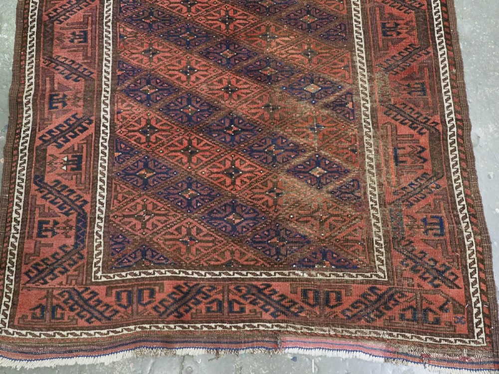 An antique 19th-century Khorasan Baluch wool rug featuring a repeating diamond calyx lattice pattern in rust red, dark navy, and brown with geometric borders. View VI