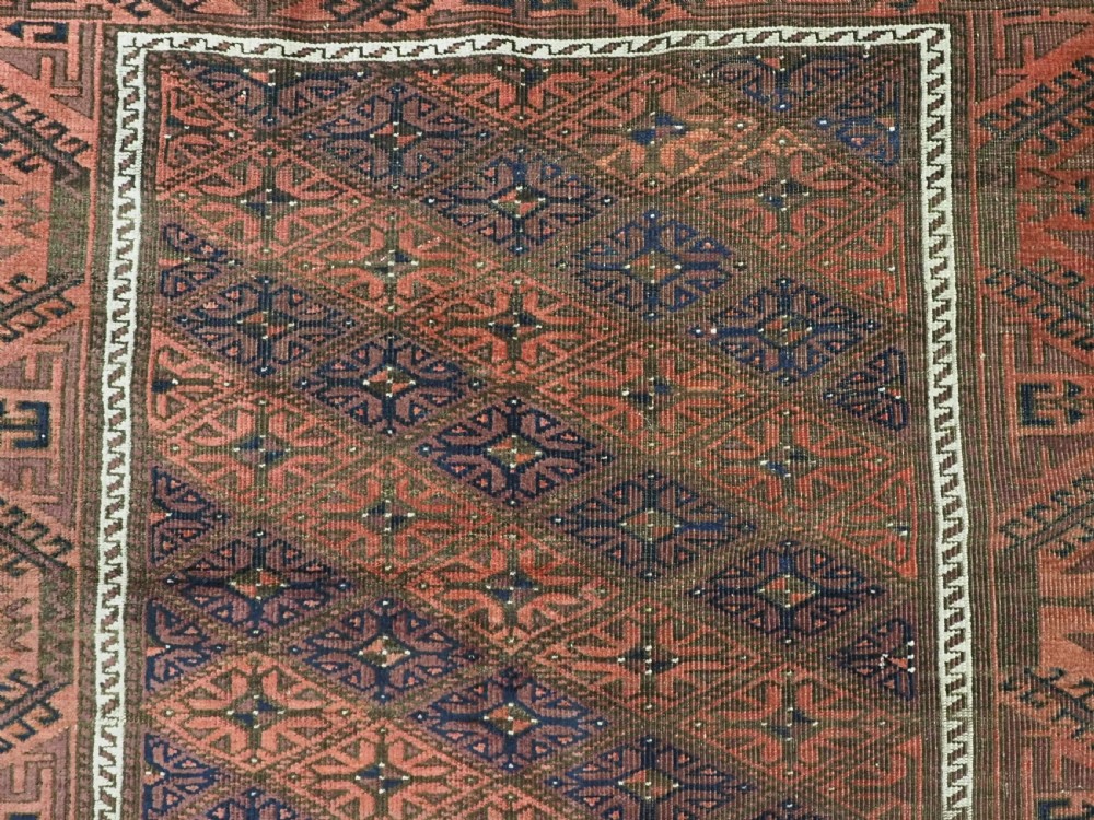 An antique 19th-century Khorasan Baluch wool rug featuring a repeating diamond calyx lattice pattern in rust red, dark navy, and brown with geometric borders. View IX