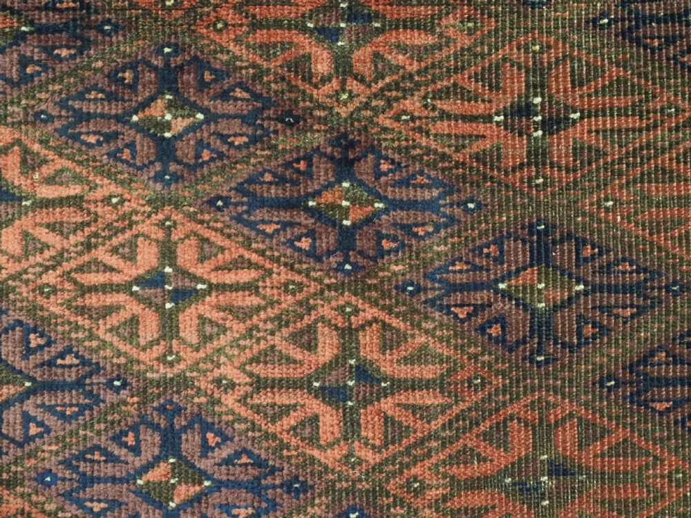 An antique 19th-century Khorasan Baluch wool rug featuring a repeating diamond calyx lattice pattern in rust red, dark navy, and brown with geometric borders. View X