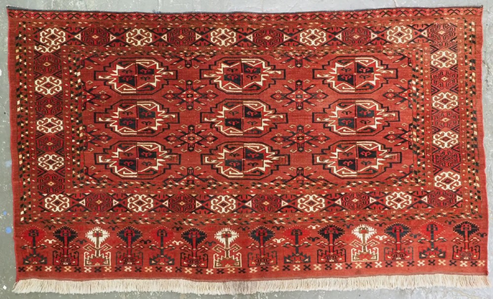 A rectangular hand-knotted red wool Turkmen chuval rug face featuring nine repeating octagonal gul motifs framed by geometric borders.
