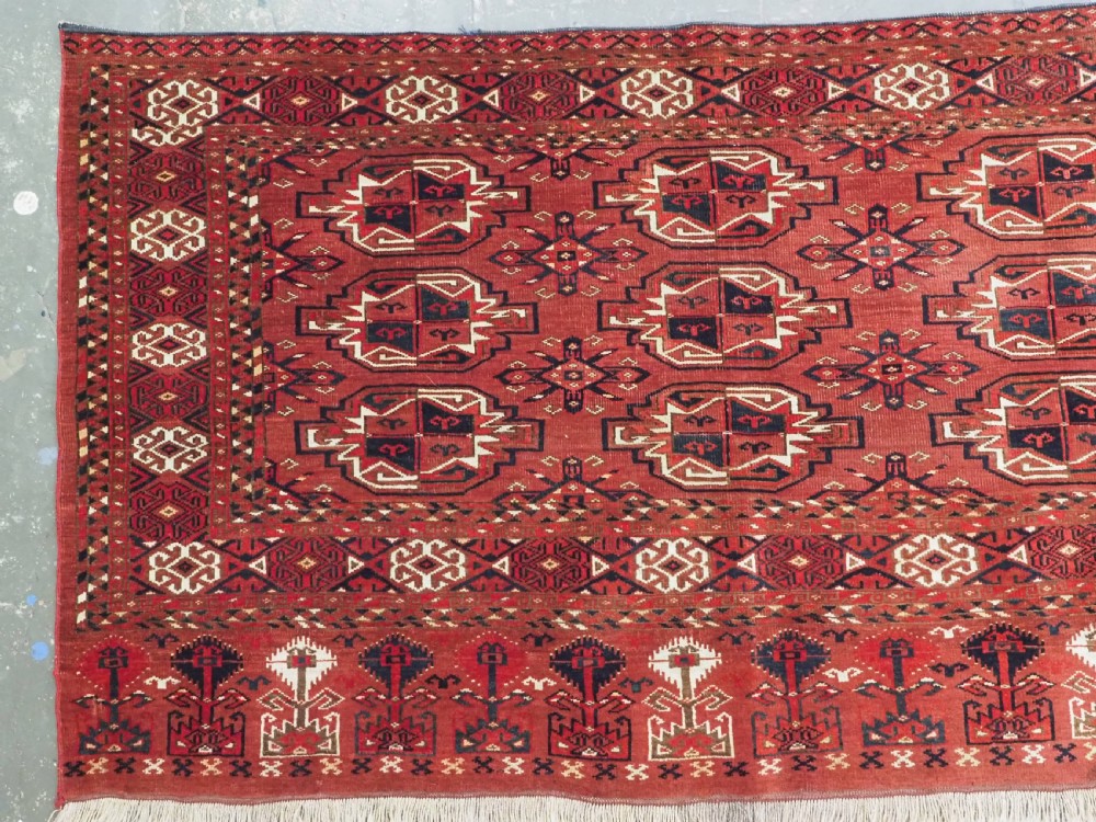 A rectangular hand-knotted red wool Turkmen chuval rug face featuring nine repeating octagonal gul motifs framed by geometric borders. View II