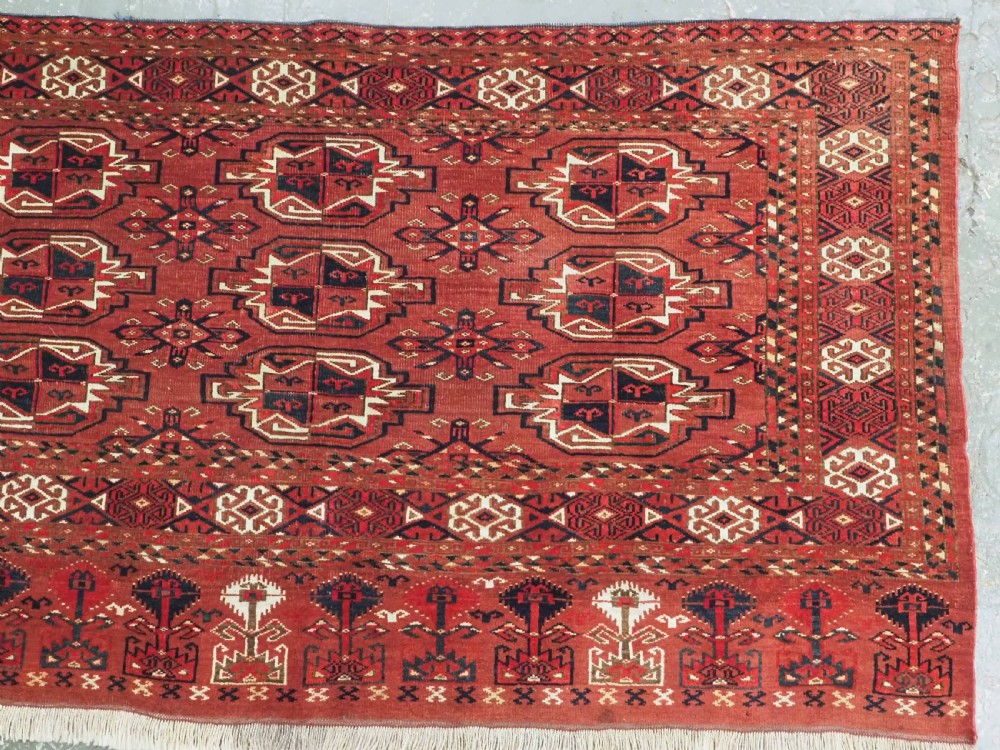 A rectangular hand-knotted red wool Turkmen chuval rug face featuring nine repeating octagonal gul motifs framed by geometric borders. View III