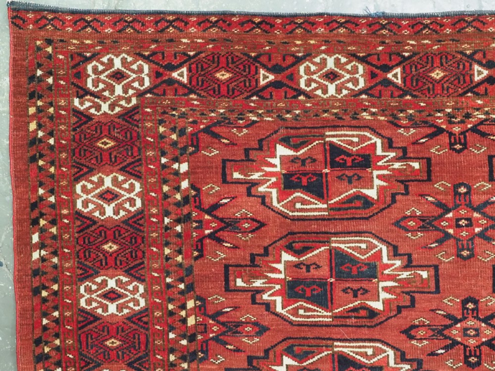 A rectangular hand-knotted red wool Turkmen chuval rug face featuring nine repeating octagonal gul motifs framed by geometric borders. View IV