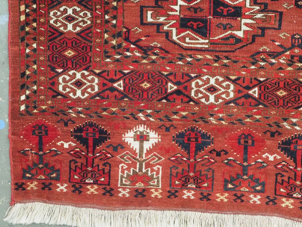 A rectangular hand-knotted red wool Turkmen chuval rug face featuring nine repeating octagonal gul motifs framed by geometric borders. View V