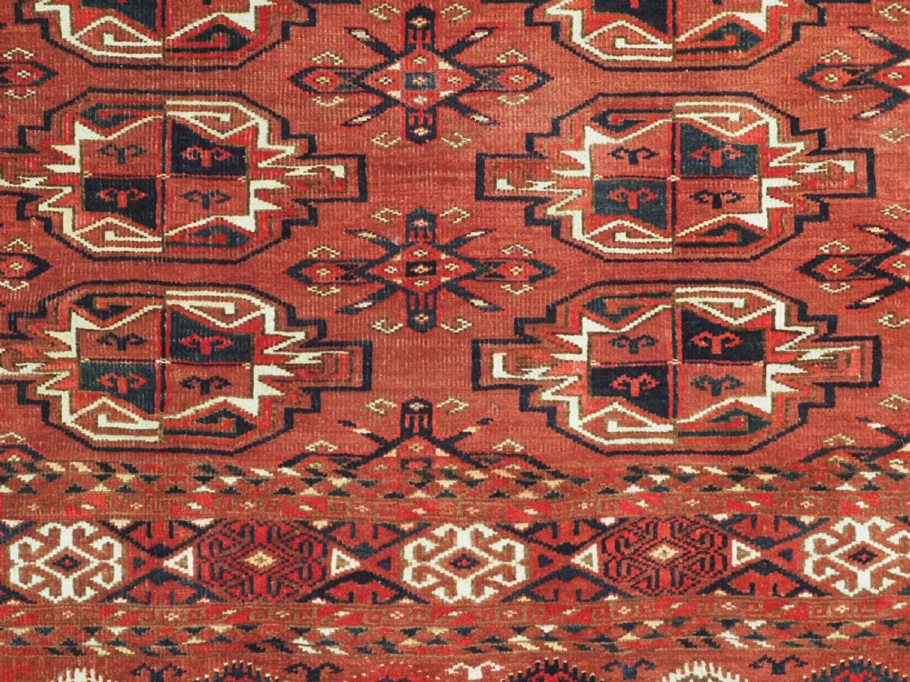 A rectangular hand-knotted red wool Turkmen chuval rug face featuring nine repeating octagonal gul motifs framed by geometric borders. View VII