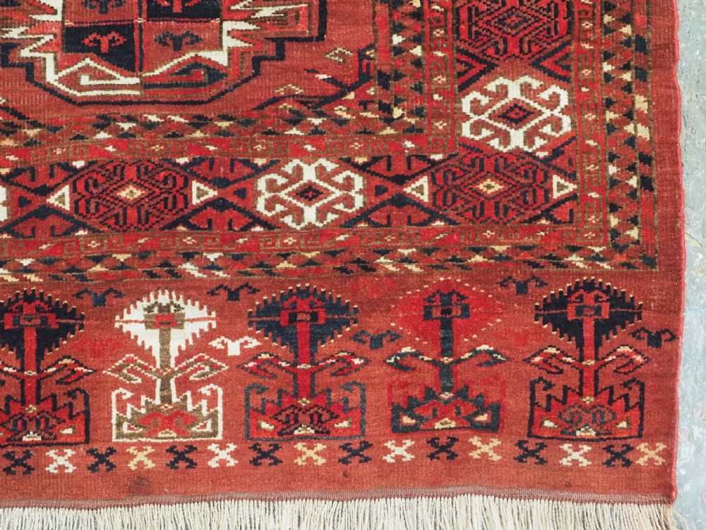 A rectangular hand-knotted red wool Turkmen chuval rug face featuring nine repeating octagonal gul motifs framed by geometric borders. View IX