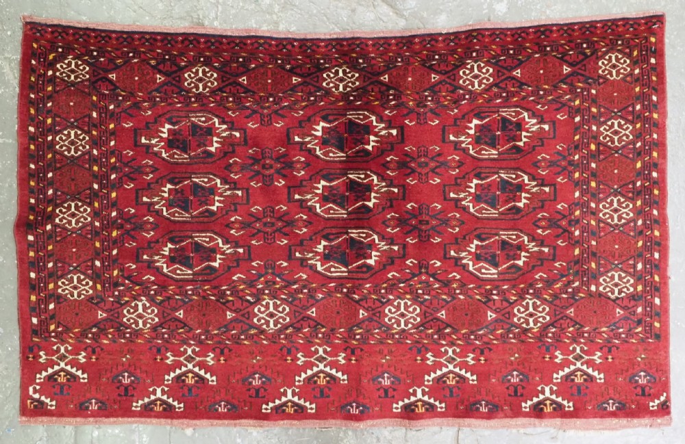 An antique hand-knotted Ersari Kizil Ayak Turkmen chuval face featuring nine octagonal guls on a deep red wool field with geometric borders.