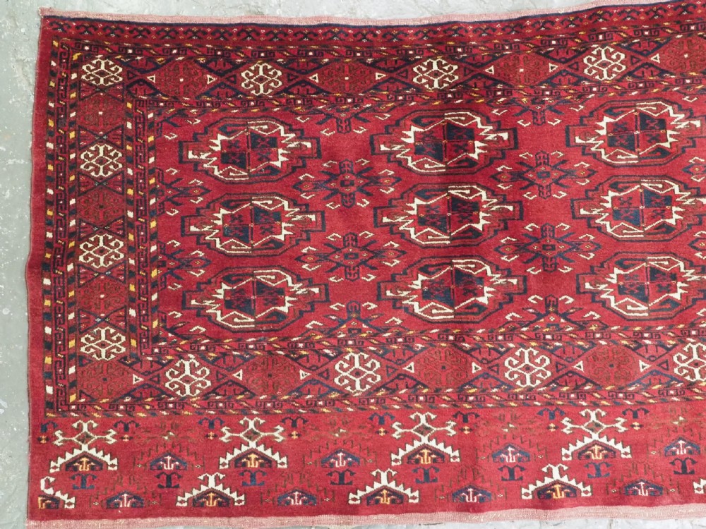 An antique hand-knotted Ersari Kizil Ayak Turkmen chuval face featuring nine octagonal guls on a deep red wool field with geometric borders. View III