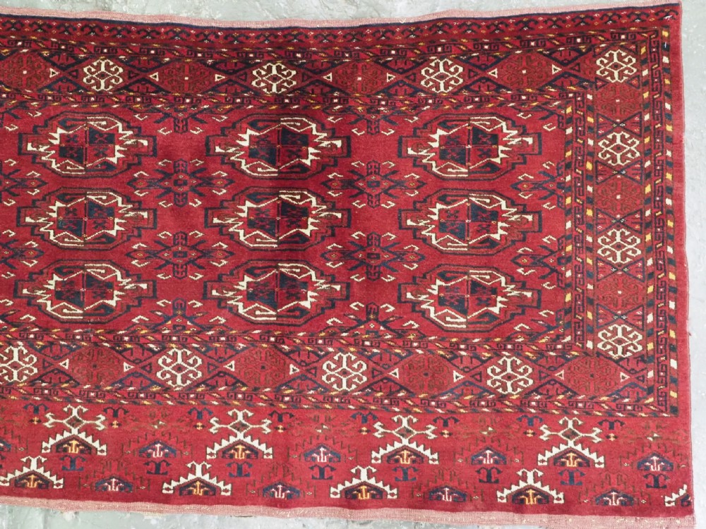 An antique hand-knotted Ersari Kizil Ayak Turkmen chuval face featuring nine octagonal guls on a deep red wool field with geometric borders. View IV