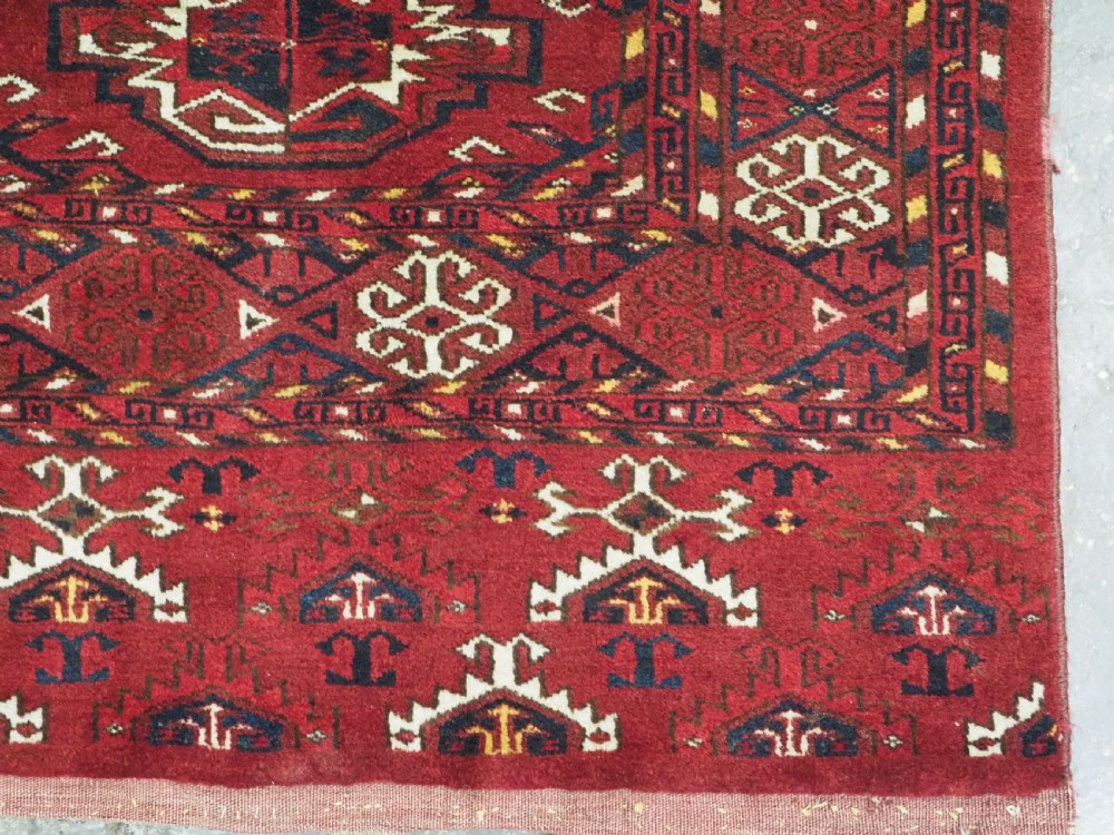 An antique hand-knotted Ersari Kizil Ayak Turkmen chuval face featuring nine octagonal guls on a deep red wool field with geometric borders. View X