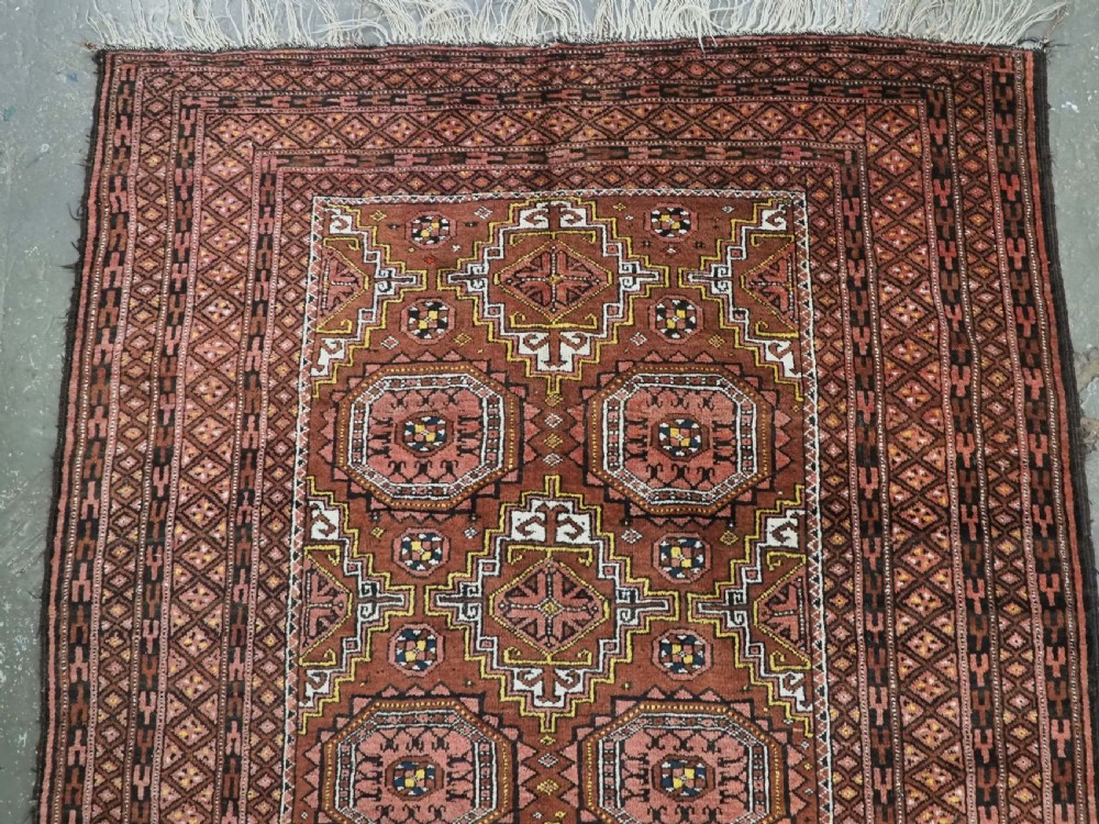 An antique hand-woven Salar Khani Baluch wool rug featuring geometric octagonal gul motifs in rust red, terracotta, and dark brown tones. View IV