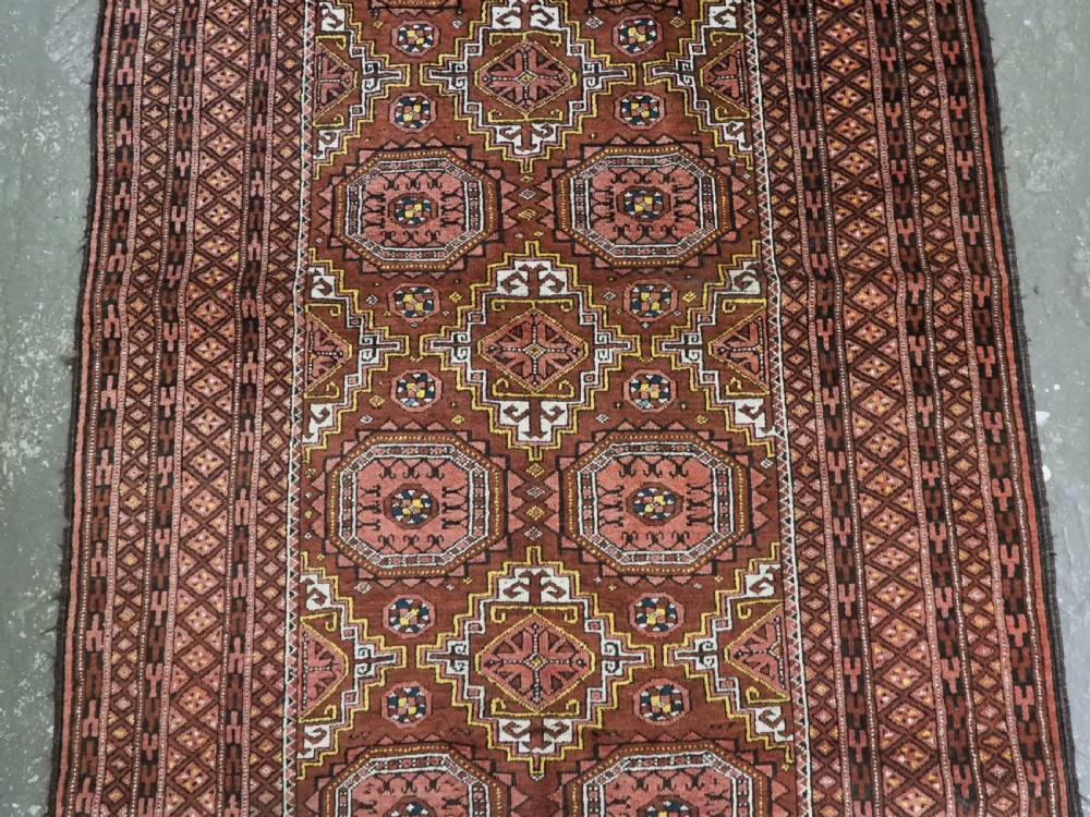 An antique hand-woven Salar Khani Baluch wool rug featuring geometric octagonal gul motifs in rust red, terracotta, and dark brown tones. View V