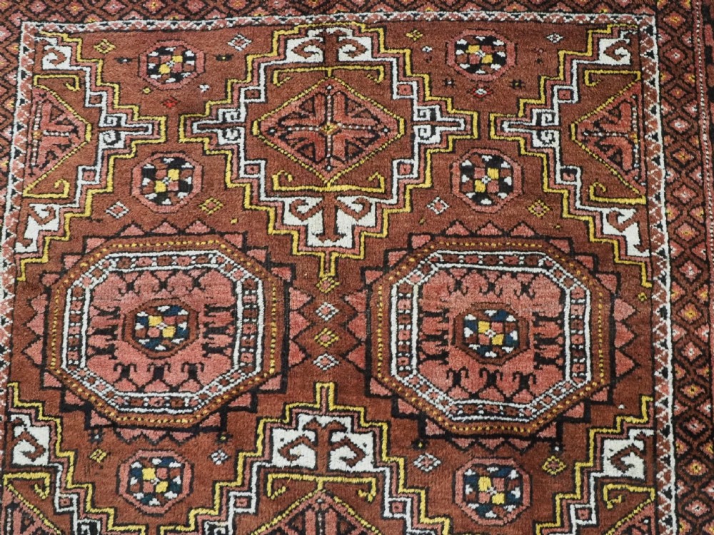 An antique hand-woven Salar Khani Baluch wool rug featuring geometric octagonal gul motifs in rust red, terracotta, and dark brown tones. View IX