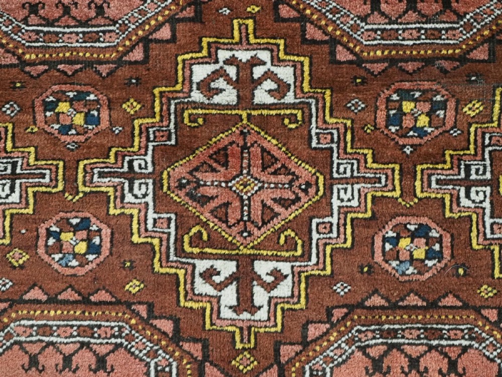 An antique hand-woven Salar Khani Baluch wool rug featuring geometric octagonal gul motifs in rust red, terracotta, and dark brown tones. View X