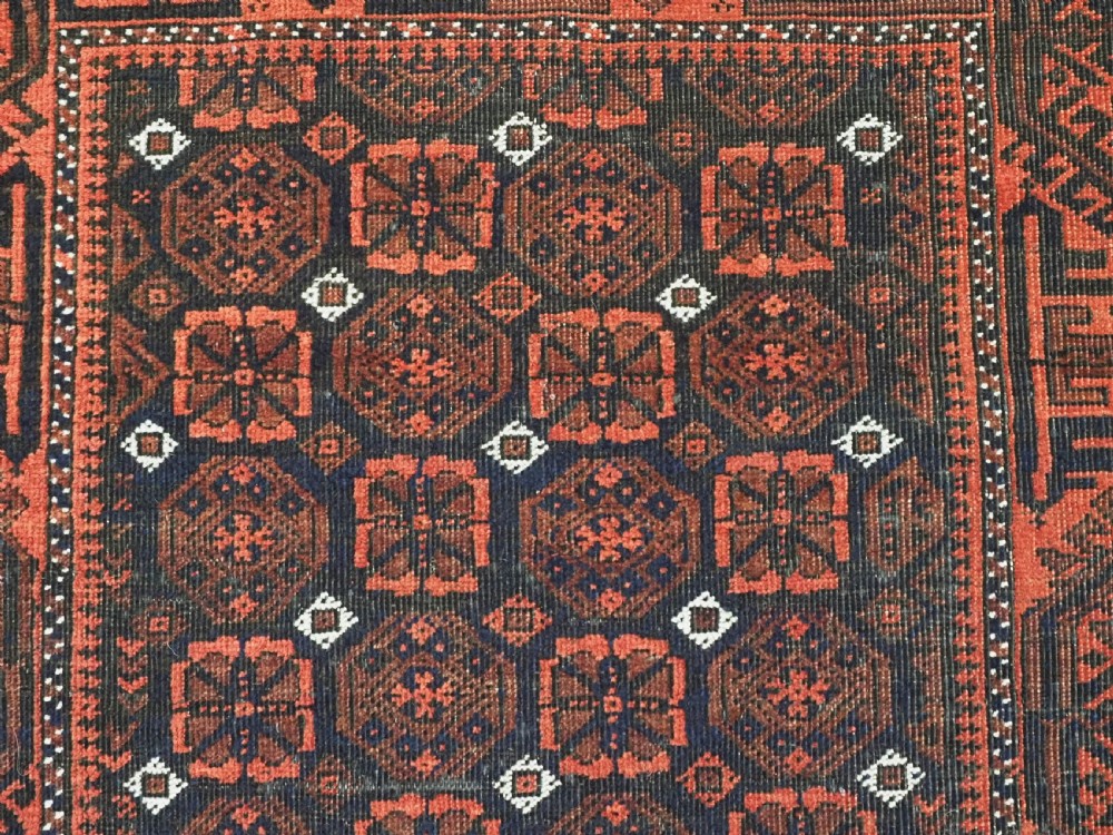 An antique handwoven Baluch rug featuring a dark central field with repeating geometric floral motifs and a wide terracotta red border. View VII