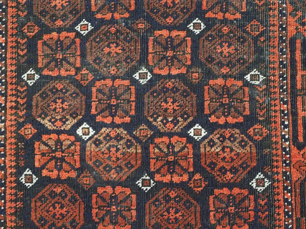 An antique handwoven Baluch rug featuring a dark central field with repeating geometric floral motifs and a wide terracotta red border. View VIII
