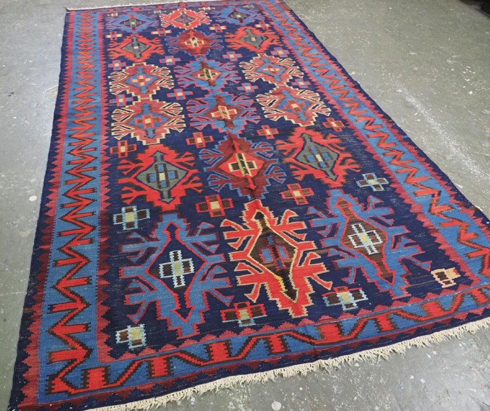 An antique flatweave Caucasian Kuba kilim rug featuring geometric shield medallions in red, blue, and cream across a dark navy field. View II
