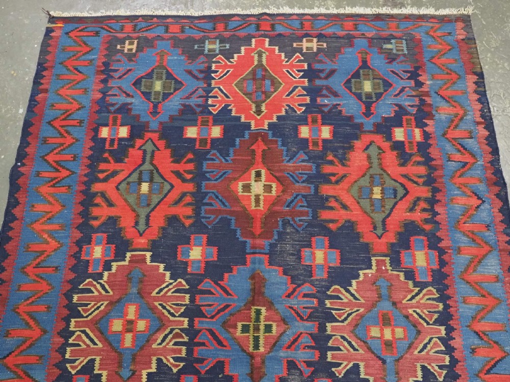 An antique flatweave Caucasian Kuba kilim rug featuring geometric shield medallions in red, blue, and cream across a dark navy field. View III