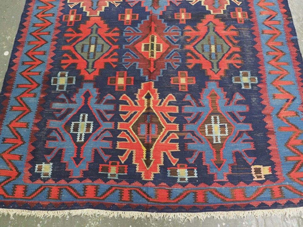 An antique flatweave Caucasian Kuba kilim rug featuring geometric shield medallions in red, blue, and cream across a dark navy field. View V