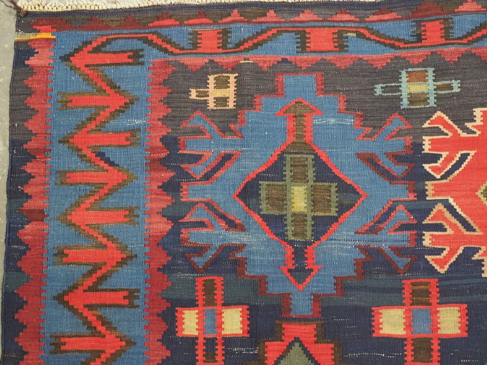 An antique flatweave Caucasian Kuba kilim rug featuring geometric shield medallions in red, blue, and cream across a dark navy field. View VI