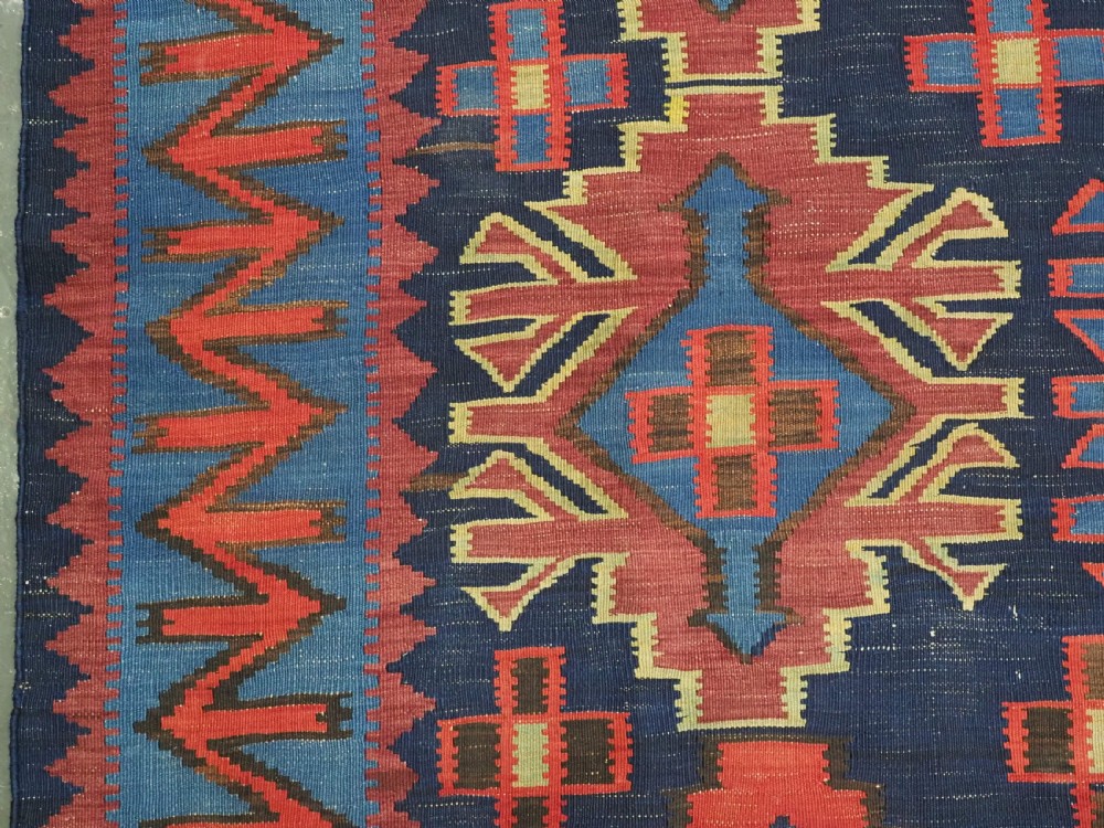 An antique flatweave Caucasian Kuba kilim rug featuring geometric shield medallions in red, blue, and cream across a dark navy field. View VII
