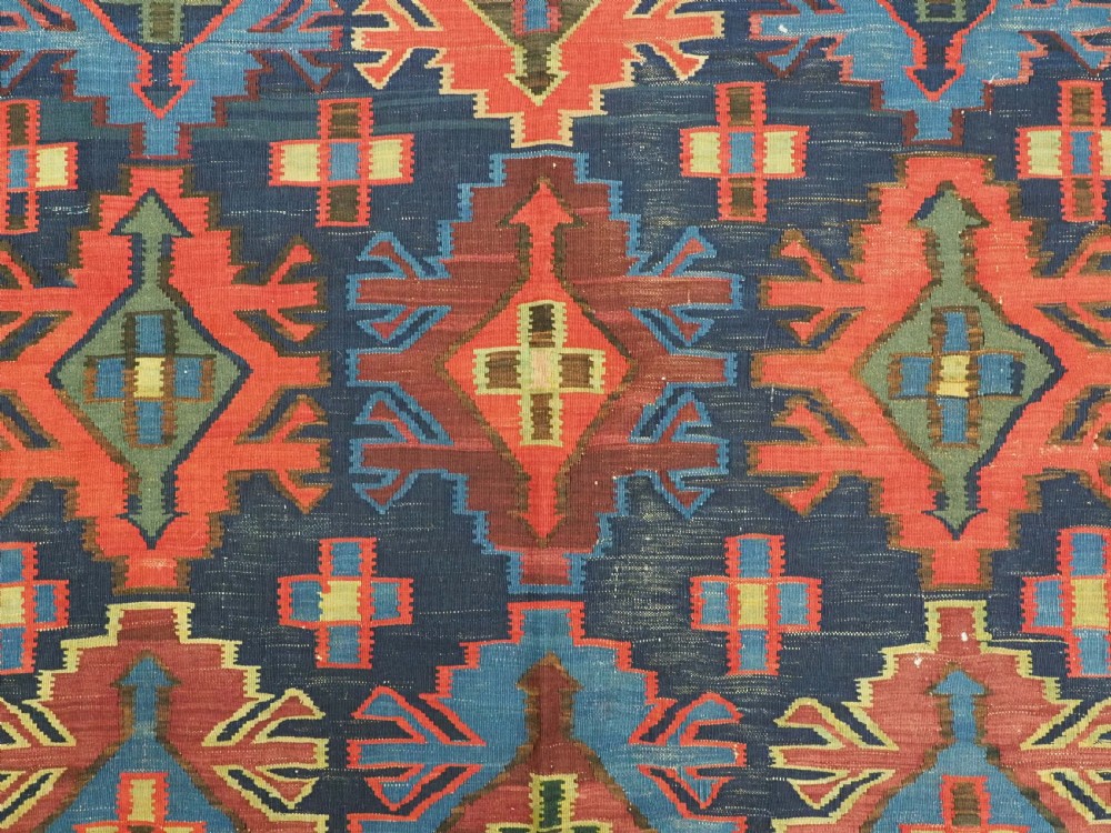 An antique flatweave Caucasian Kuba kilim rug featuring geometric shield medallions in red, blue, and cream across a dark navy field. View VIII