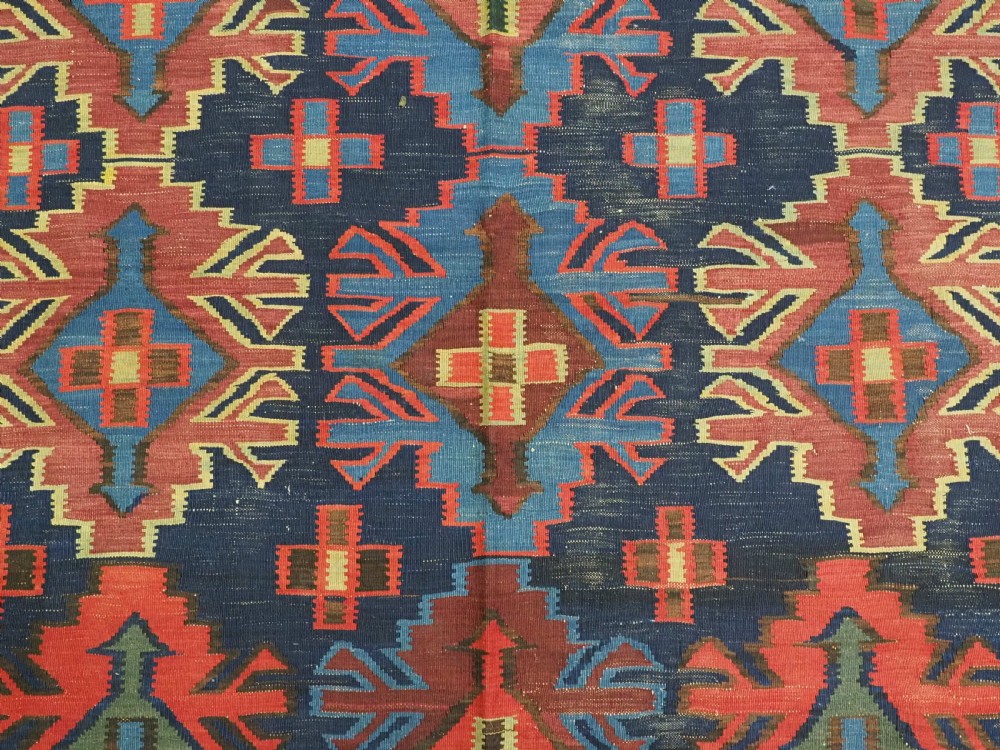 An antique flatweave Caucasian Kuba kilim rug featuring geometric shield medallions in red, blue, and cream across a dark navy field. View IX