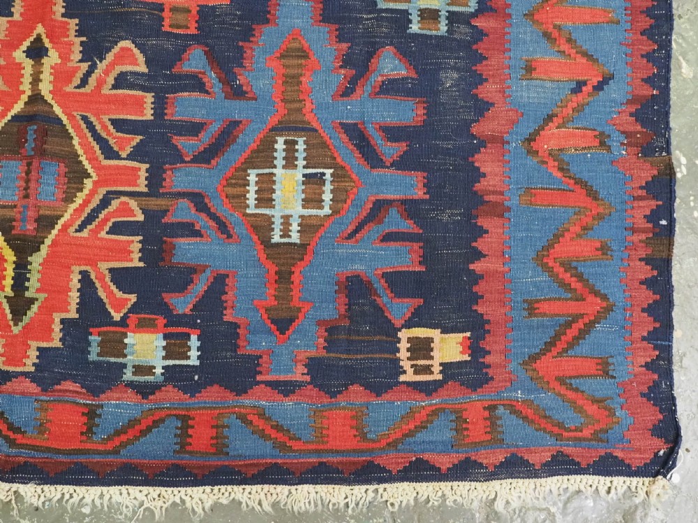 An antique flatweave Caucasian Kuba kilim rug featuring geometric shield medallions in red, blue, and cream across a dark navy field. View XI