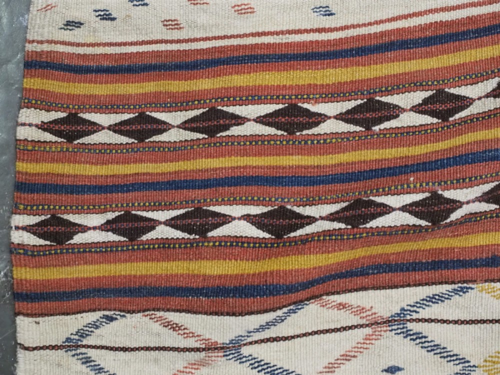 A flatwoven wool kilim rug featuring horizontal bands of cream, dark brown, and ochre with geometric diamond patterns. View X