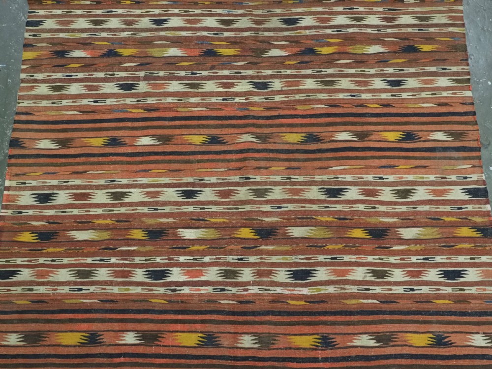 A long handwoven flatweave wool runner rug featuring horizontal bands of terracotta, dark brown, yellow, and cream geometric patterns. View IV