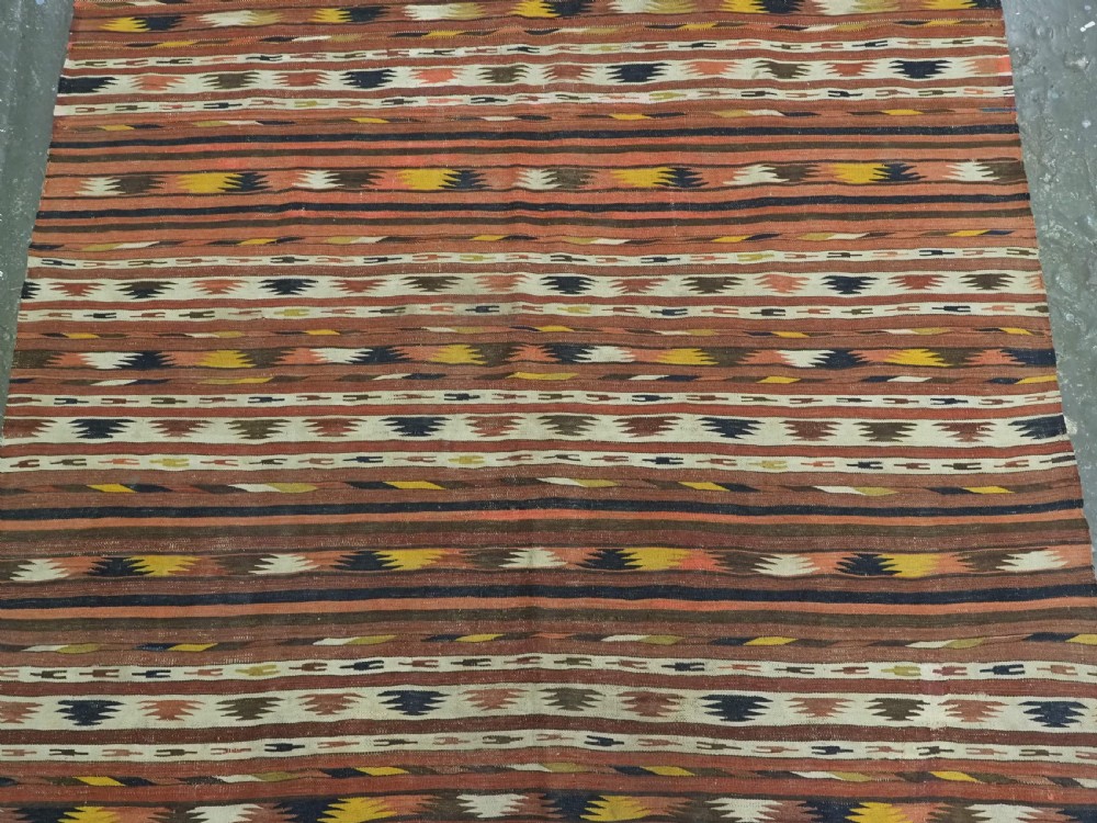 A long handwoven flatweave wool runner rug featuring horizontal bands of terracotta, dark brown, yellow, and cream geometric patterns. View V