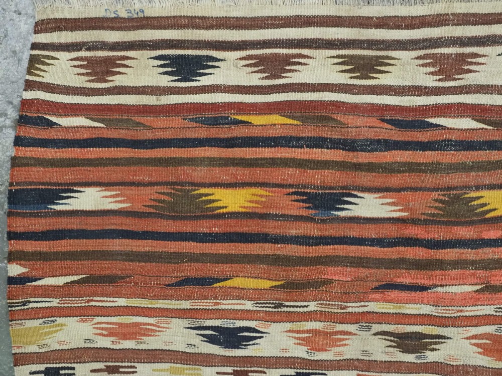 A long handwoven flatweave wool runner rug featuring horizontal bands of terracotta, dark brown, yellow, and cream geometric patterns. View VII