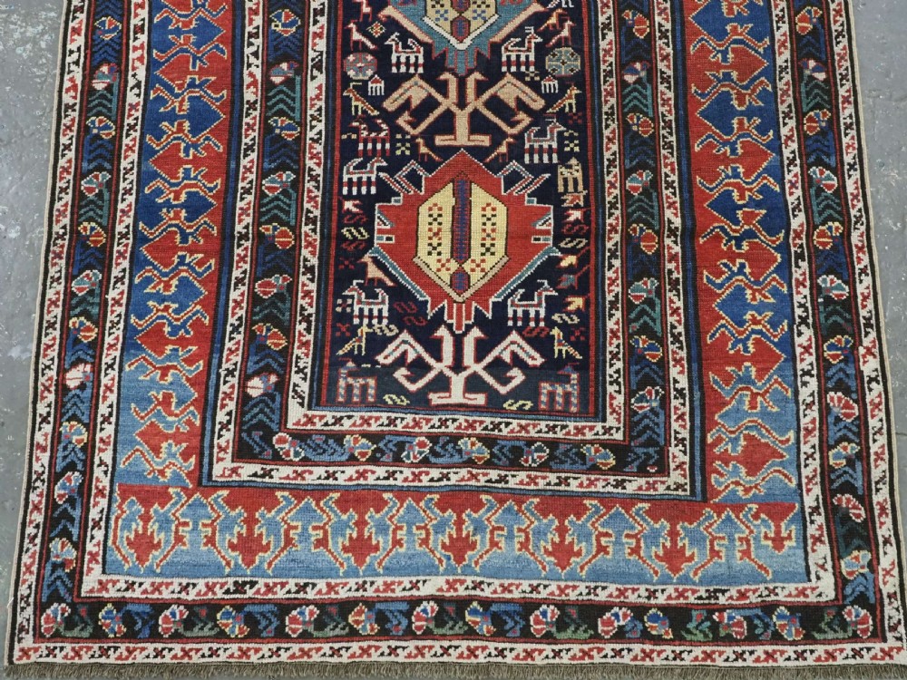 An antique late nineteenth-century Caucasian Kuba runner featuring geometric medallions and stylised animal motifs in navy blue, red, and cream wool. View V
