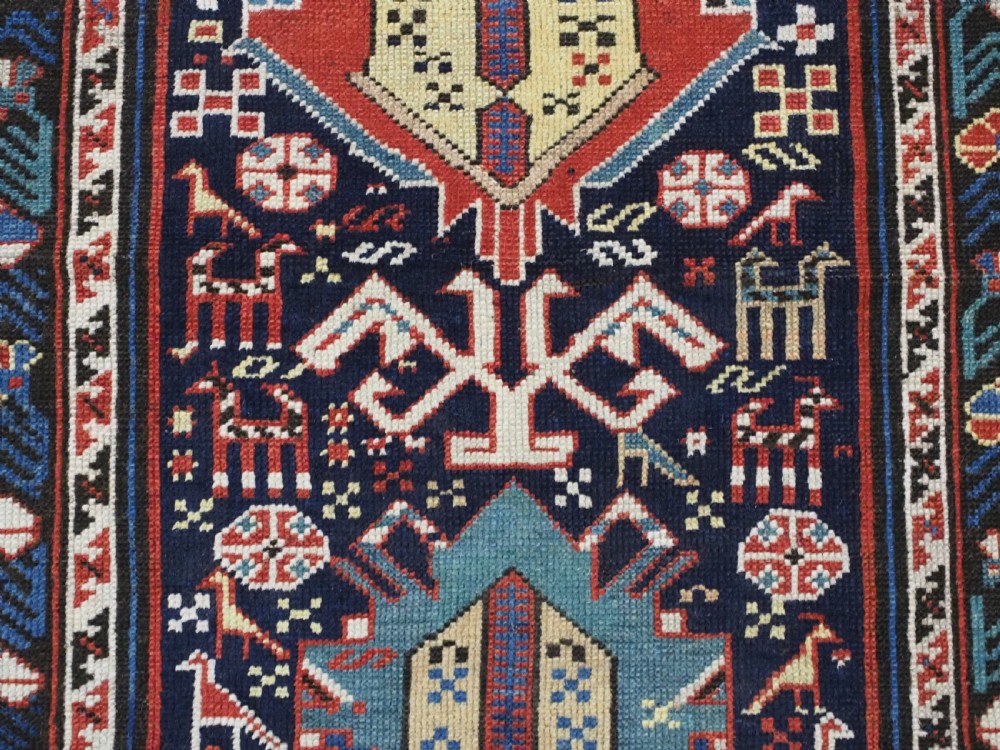 An antique late nineteenth-century Caucasian Kuba runner featuring geometric medallions and stylised animal motifs in navy blue, red, and cream wool. View X