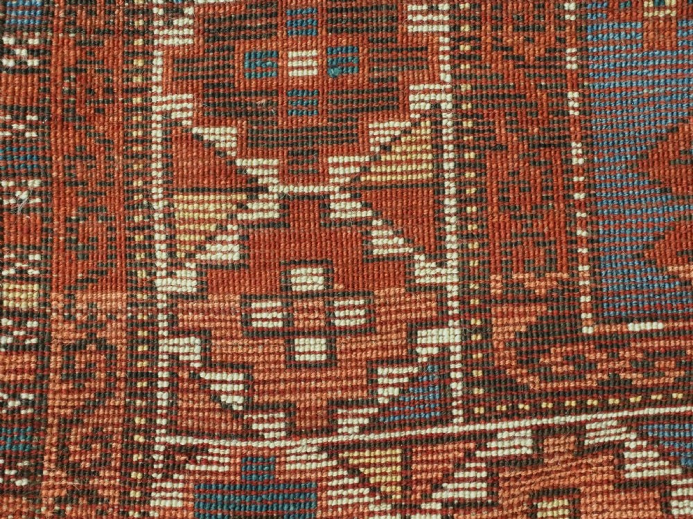 An antique hand-knotted wool rug featuring three hooked diamond medallions along a central blue field surrounded by geometric patterned borders in terracotta, red, and cream. View XIII