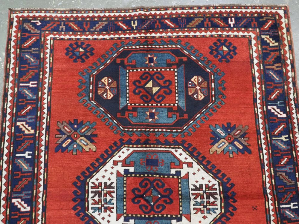 An antique Caucasian Kazak hand-knotted wool rug featuring three large geometric medallions along a rich red field surrounded by a dark blue border. View III