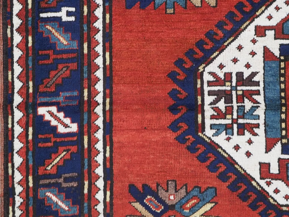 An antique Caucasian Kazak hand-knotted wool rug featuring three large geometric medallions along a rich red field surrounded by a dark blue border. View VII