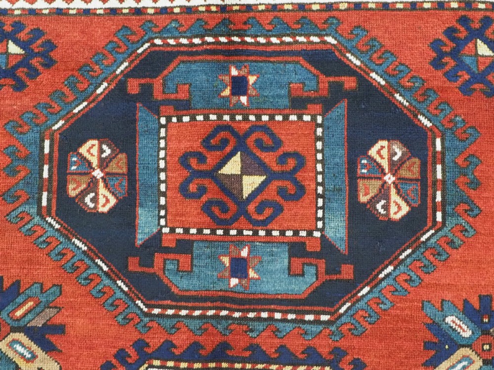 An antique Caucasian Kazak hand-knotted wool rug featuring three large geometric medallions along a rich red field surrounded by a dark blue border. View VIII