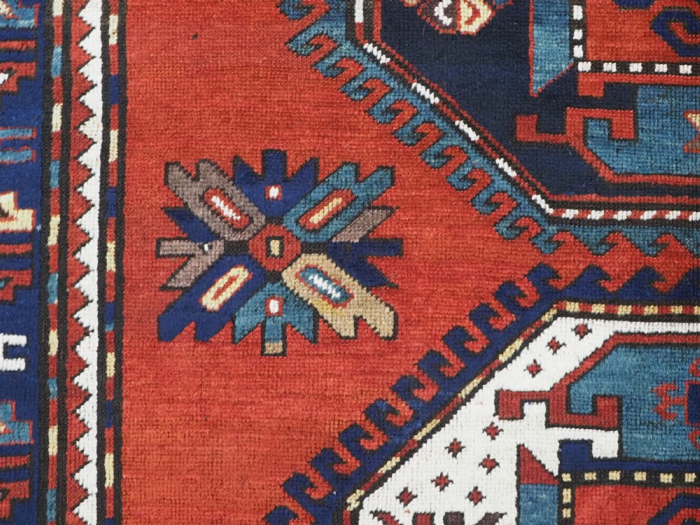 An antique Caucasian Kazak hand-knotted wool rug featuring three large geometric medallions along a rich red field surrounded by a dark blue border. View IX