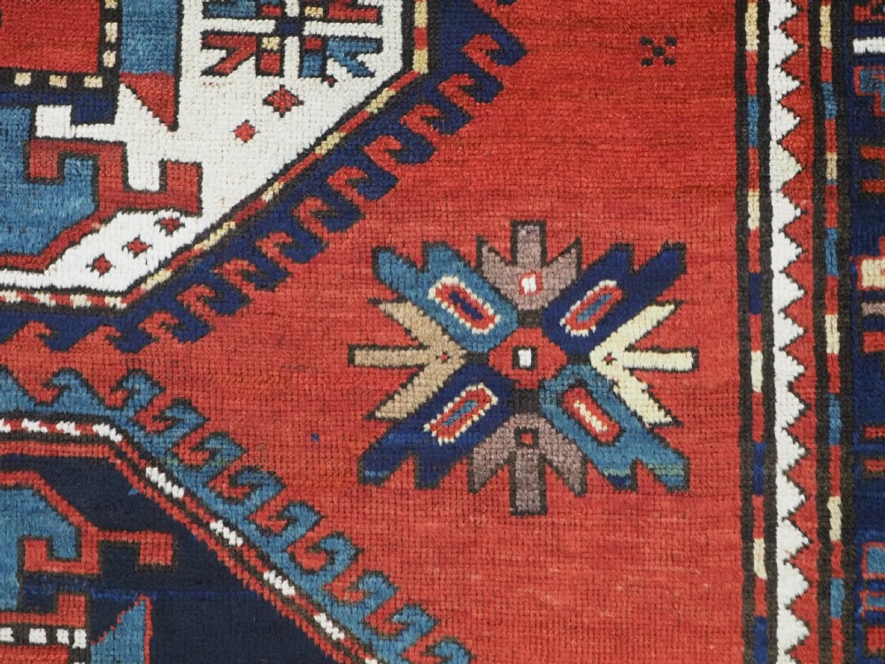 An antique Caucasian Kazak hand-knotted wool rug featuring three large geometric medallions along a rich red field surrounded by a dark blue border. View XI