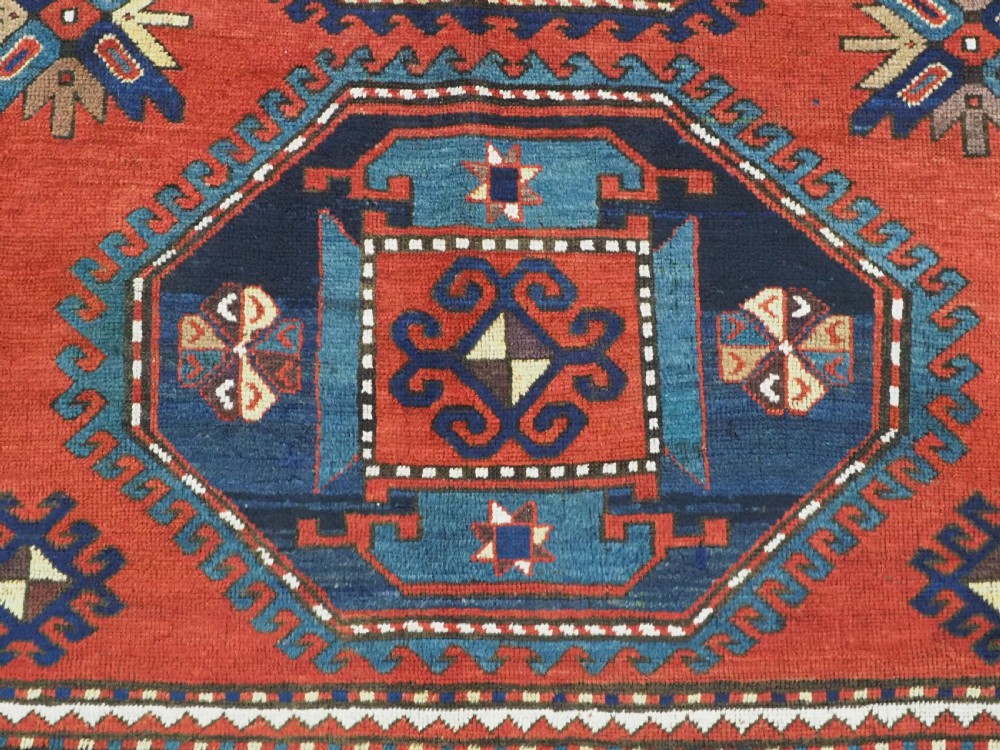 An antique Caucasian Kazak hand-knotted wool rug featuring three large geometric medallions along a rich red field surrounded by a dark blue border. View XII