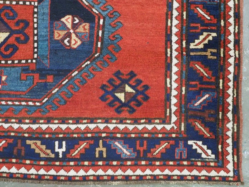 An antique Caucasian Kazak hand-knotted wool rug featuring three large geometric medallions along a rich red field surrounded by a dark blue border. View XIII
