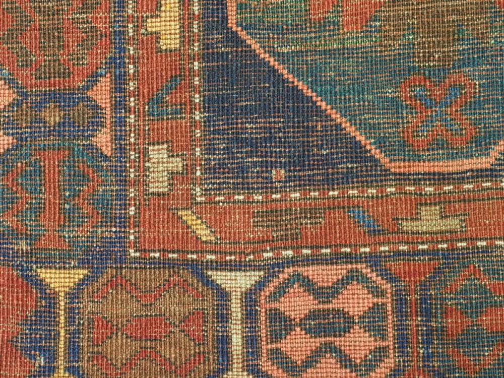 An antique hand-knotted wool rug featuring columns of red and blue hexagonal medallions on a deep navy field framed by a geometric multi-band border. View XIII