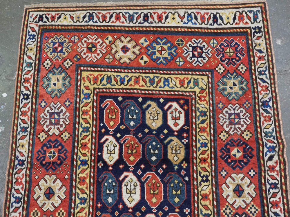 An antique hand-knotted Caucasian runner rug featuring repeated boteh motifs on a dark blue central field framed by red geometric borders. View II